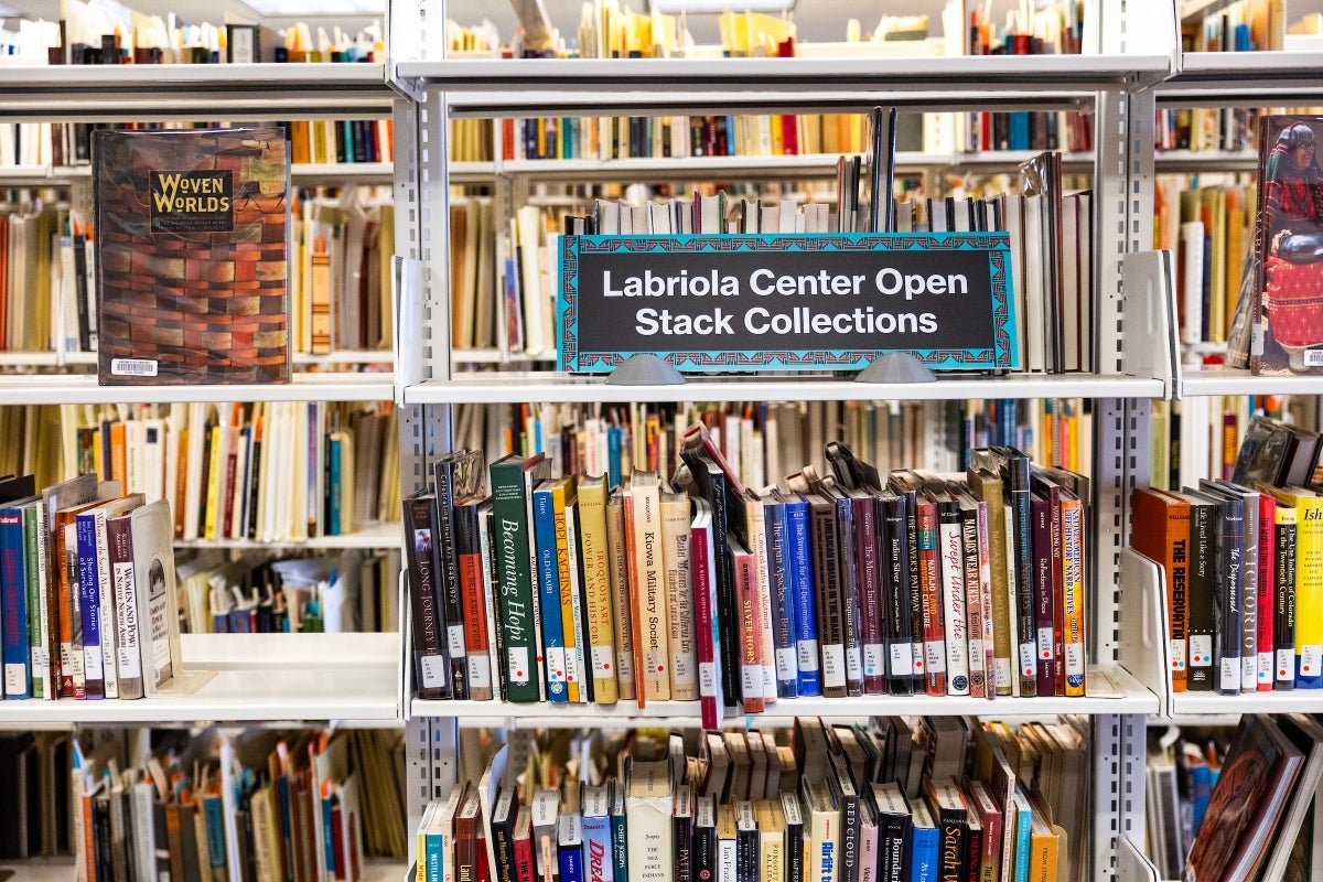 Stacks of books in a library with a sign that reads 