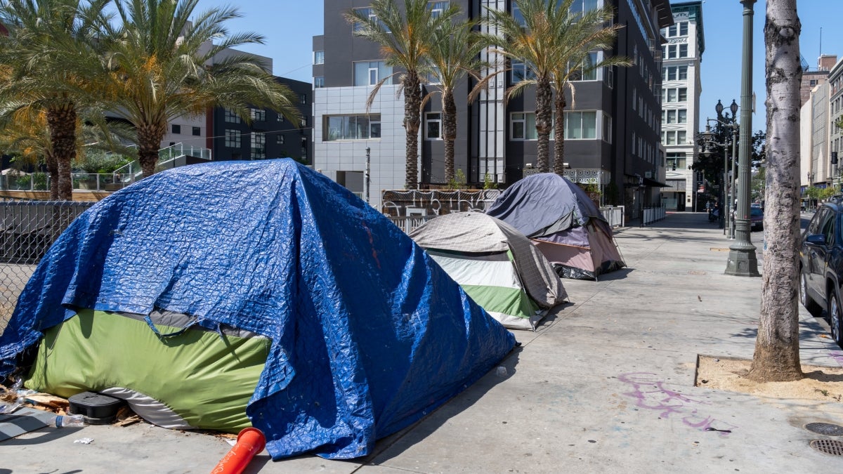 Homeless tents are set up on a city street in front of apartment buildings