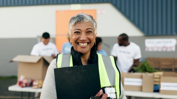 A woman smiles wearing a safety vest and holding a clipboard