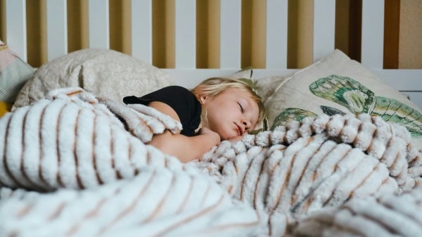 A child asleep in bed with a fluffy striped blanket and head on a pillow with a leaf pattern.