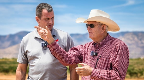 Two men mid-discussion while standing outside with a field and mountains in the backdrop