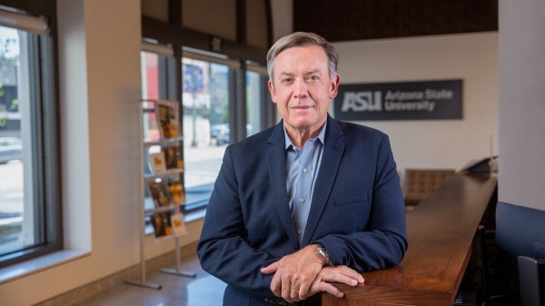 Michael Crow poses for a photo leaning against a desk
