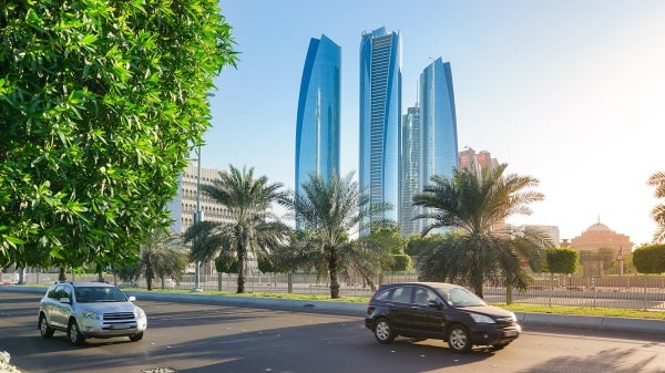 Cars travel on a street in Abu Dhabi with skyscrapers in the background.