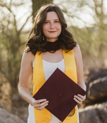 A young woman stands in graduation clothing